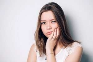 A person wearing a light sleeveless shirt is frowning and holding their jaw.