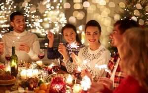 A group of people is sitting around a table with food and wine while holding lit sparklers.