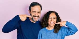 A pair of smiling people point at their own mouths.