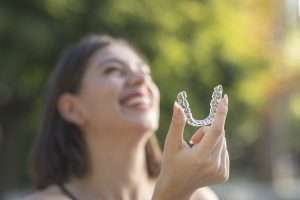 A woman smiling and holding a clear mouthguard up to the camera.